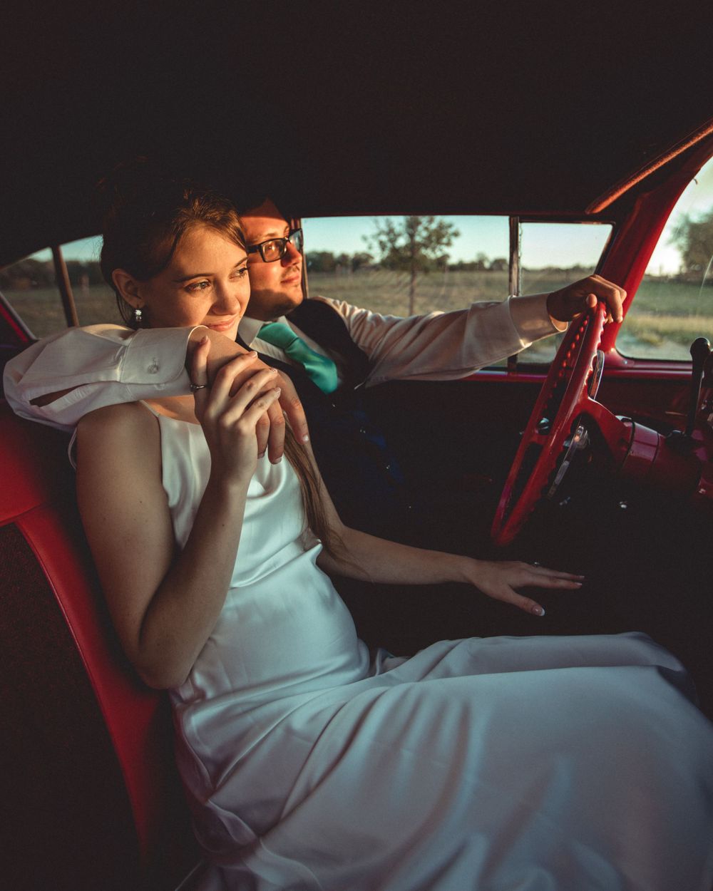Couple sits in vintage red car interior during sunset photoshoot.