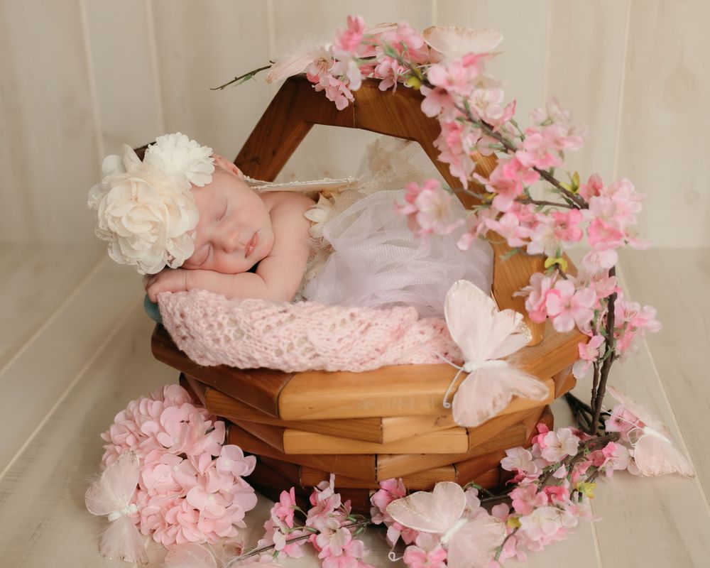 Newborn sleeping in wooden basket decorated with pink cherry blossoms and white flowers.