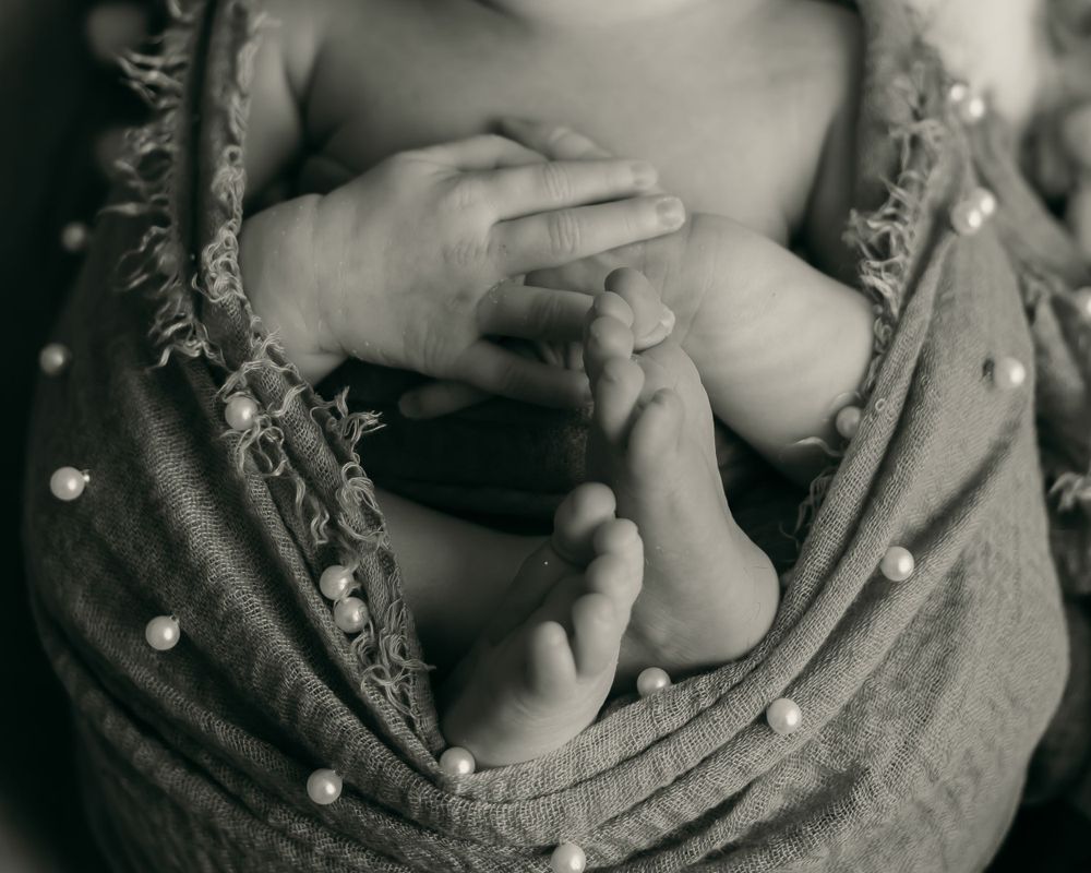 Close-up black and white photo of tiny baby feet and hands nestled in soft fabric.