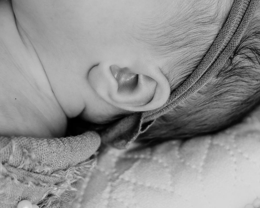 Black and white macro photograph of a baby's ear against textured fabric.