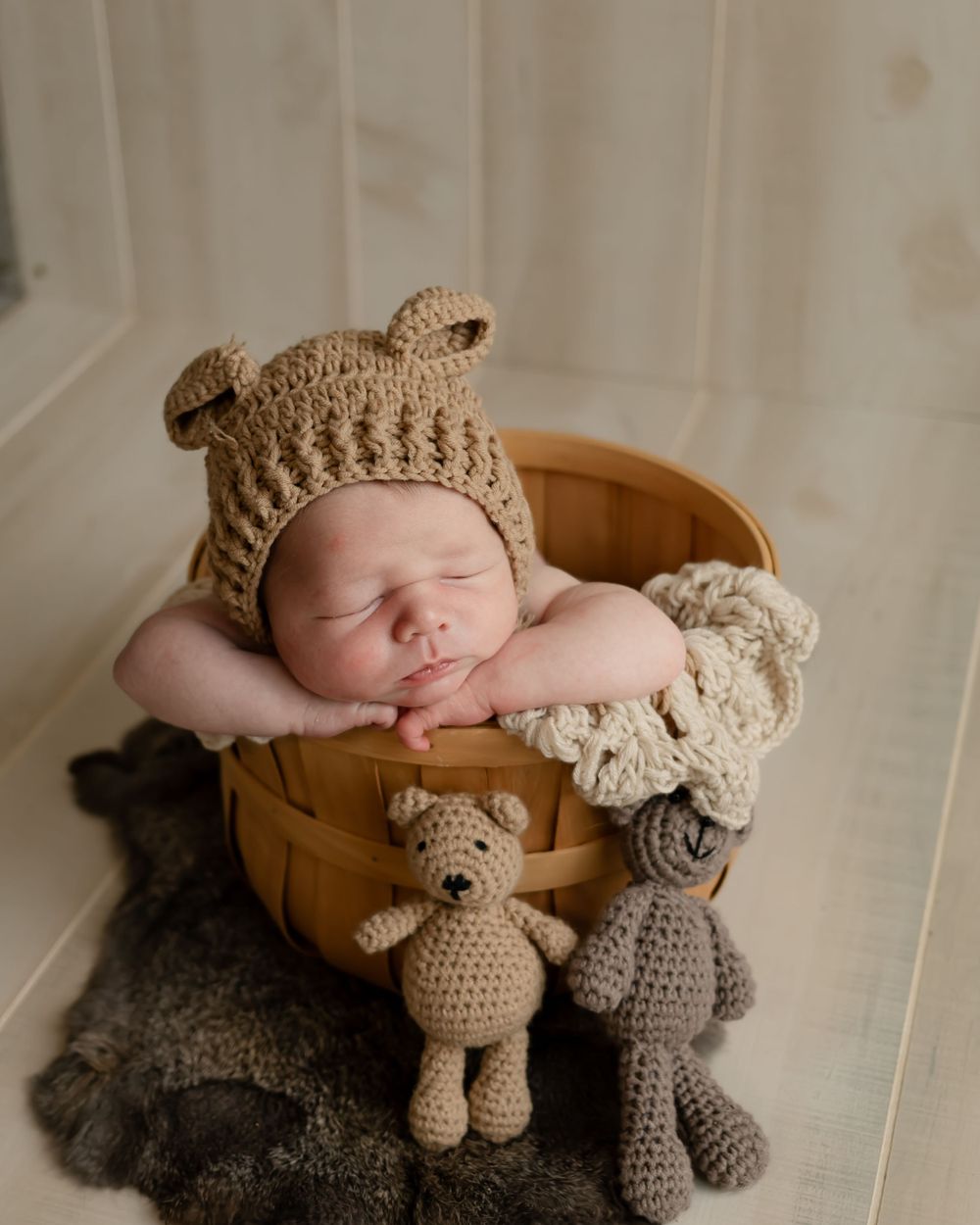 Newborn baby sleeping in wooden basket wearing bear hat with knitted stuffed animals.