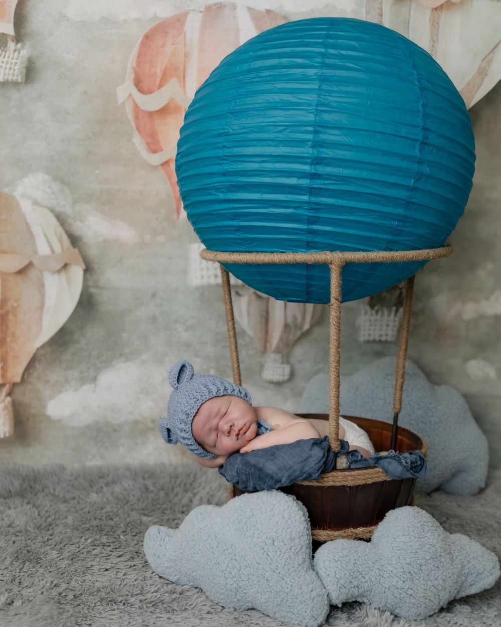Sleeping newborn in hot air balloon themed photo set with blue paper lantern and cloud props.