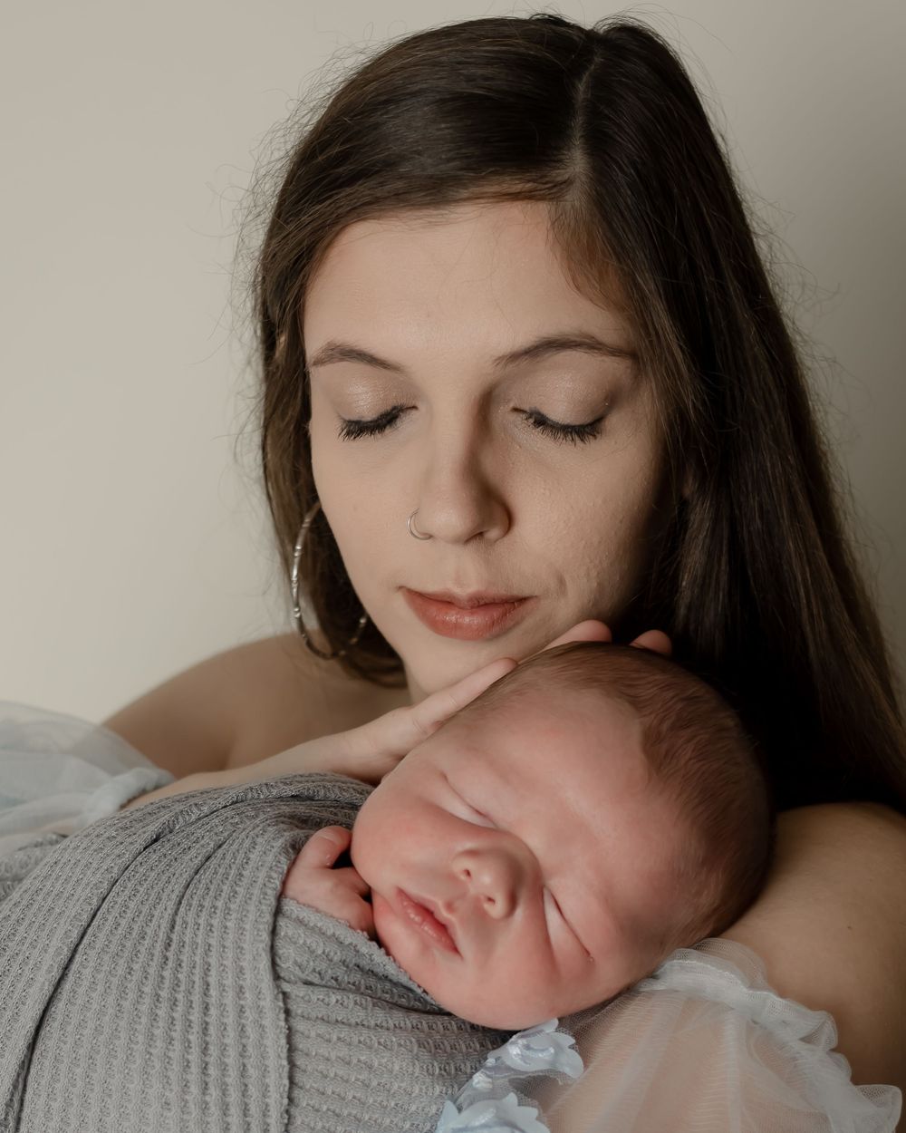 Sweet moment between mother and sleeping newborn captured in soft natural light.