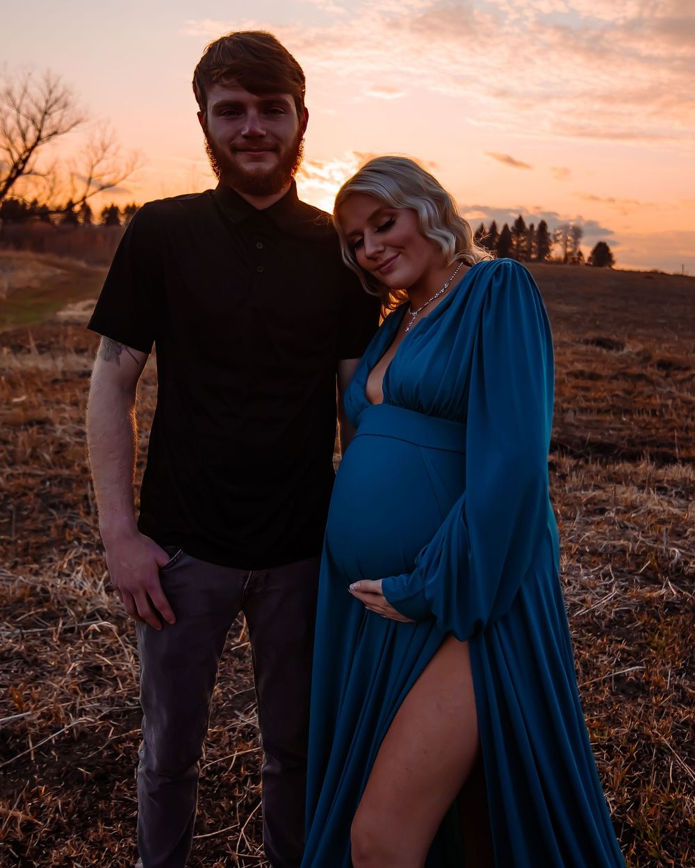 A maternity photoshoot at sunset with an elegant blue dress in a rustic field setting.