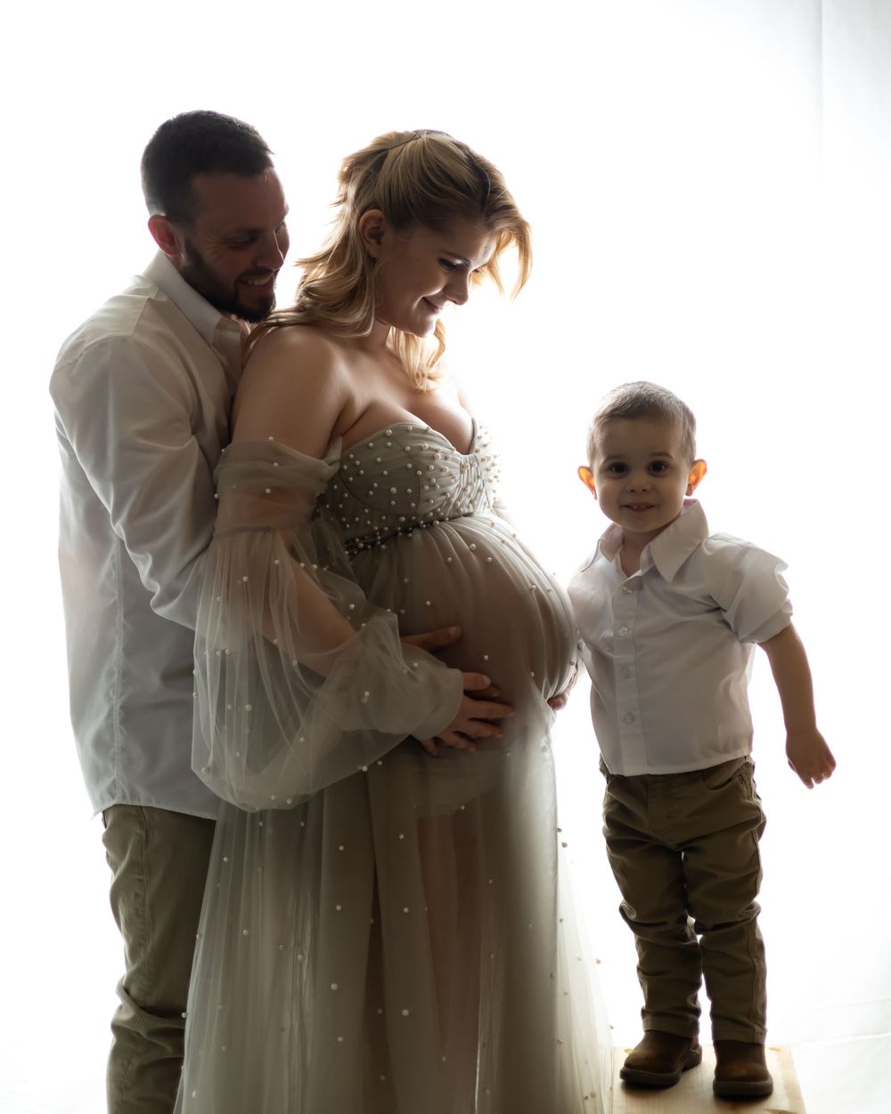Silhouetted maternity photo with family against bright window.