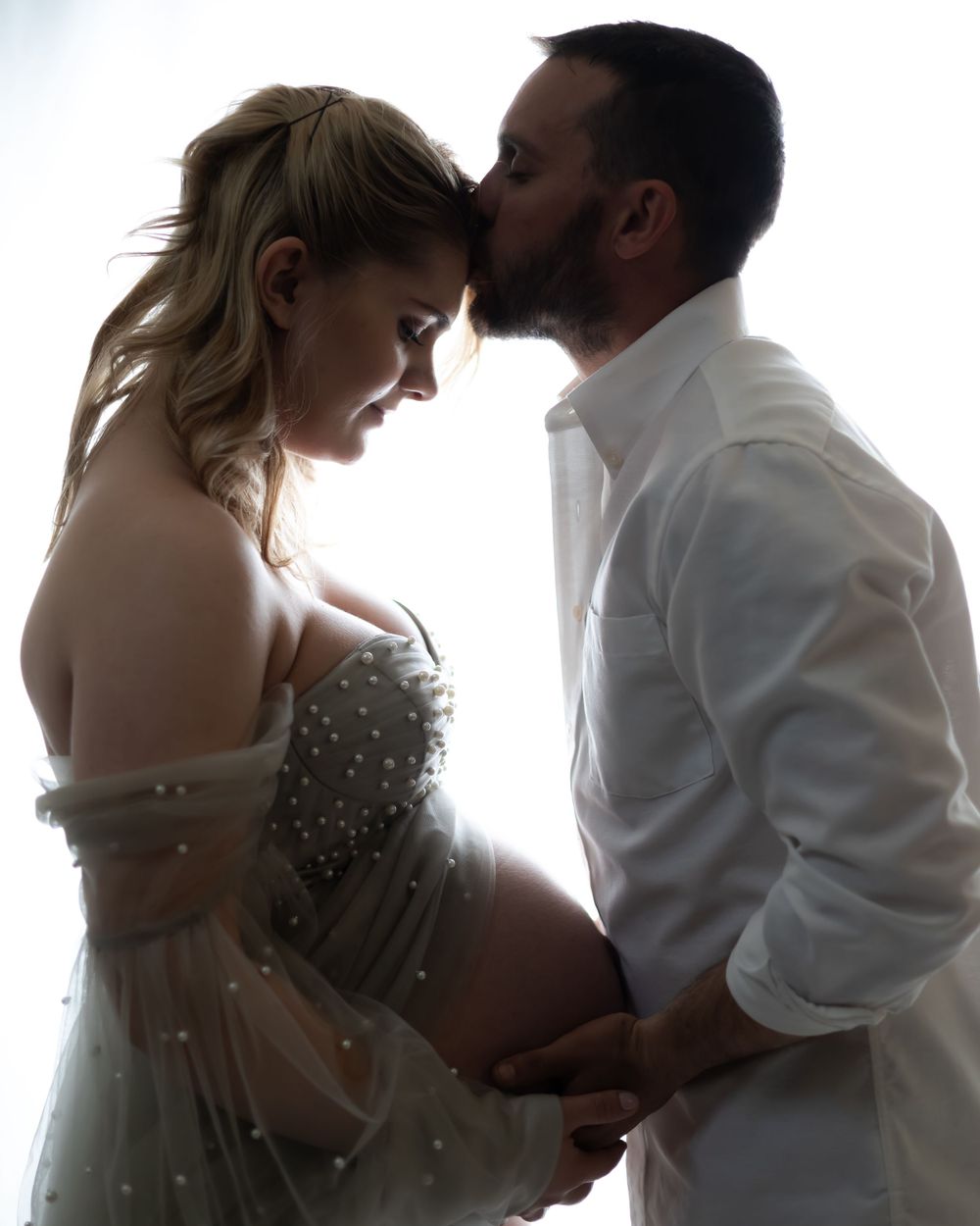 Intimate silhouette of couple embracing during maternity photoshoot.