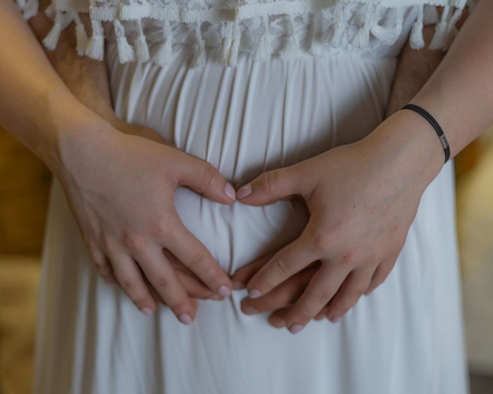 Hands forming heart shape on white dress fabric.