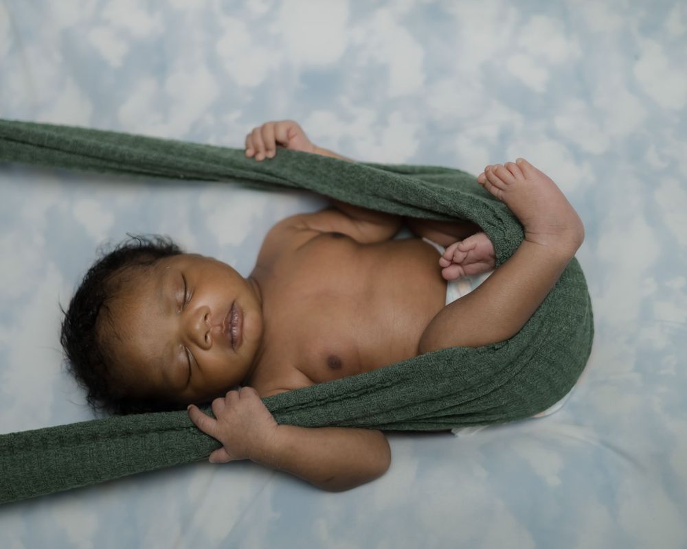 Smiling baby wrapped in green blanket lying on blue and white background.