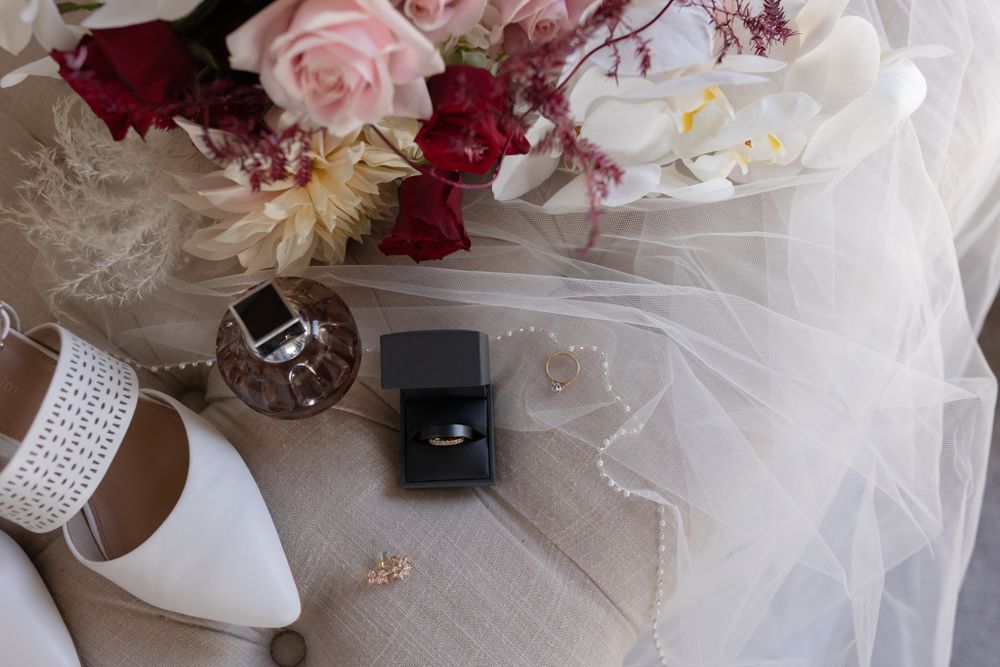 Wedding details with rings, white shoes, and pink and red floral arrangement on veil.