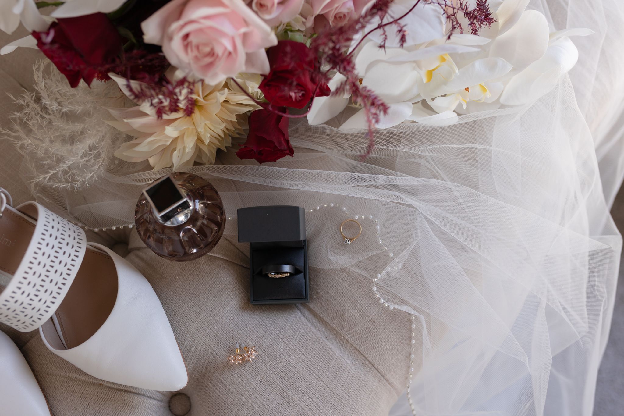 Wedding details with rings, white shoes, and pink and red floral arrangement on veil.