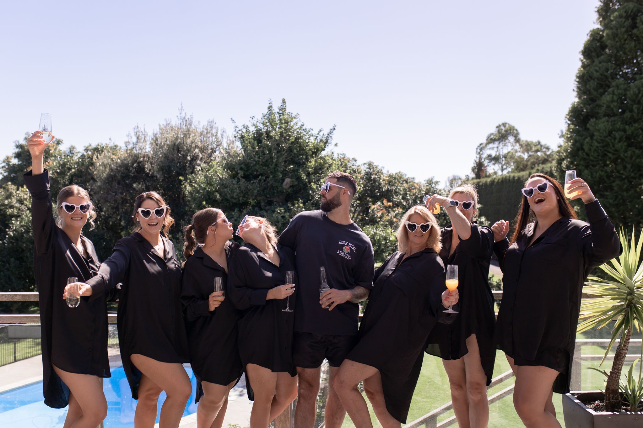 Bridal party in matching black outfits posing playfully by pool.