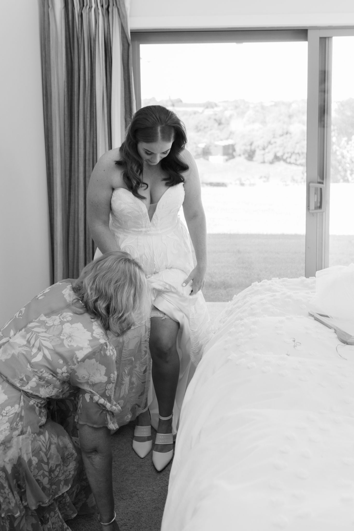A tender moment during wedding preparations as final adjustments are made to the bridal gown.