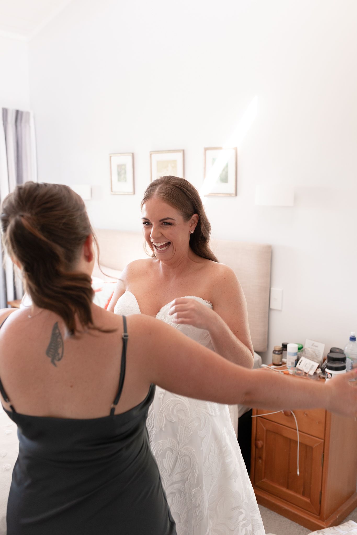 Two people share a joyful moment during wedding preparations in a bright white room.