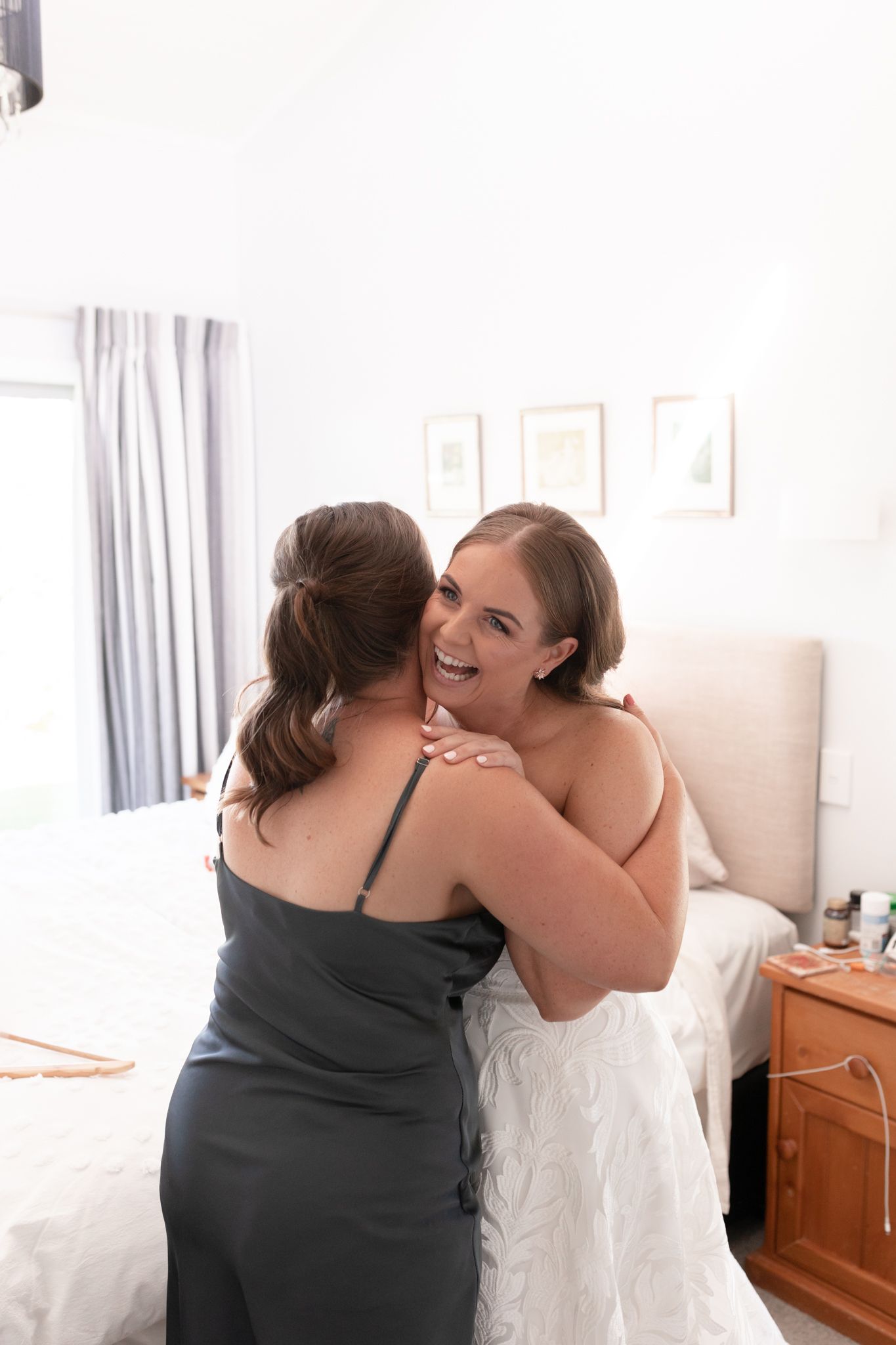 An emotional embrace captured during wedding day preparations in a sunlit room.