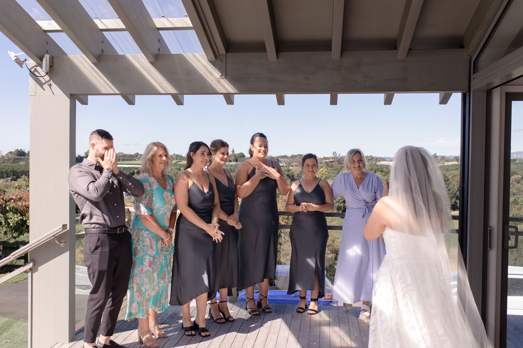 Wedding party stands together on a covered patio with scenic views in the background.