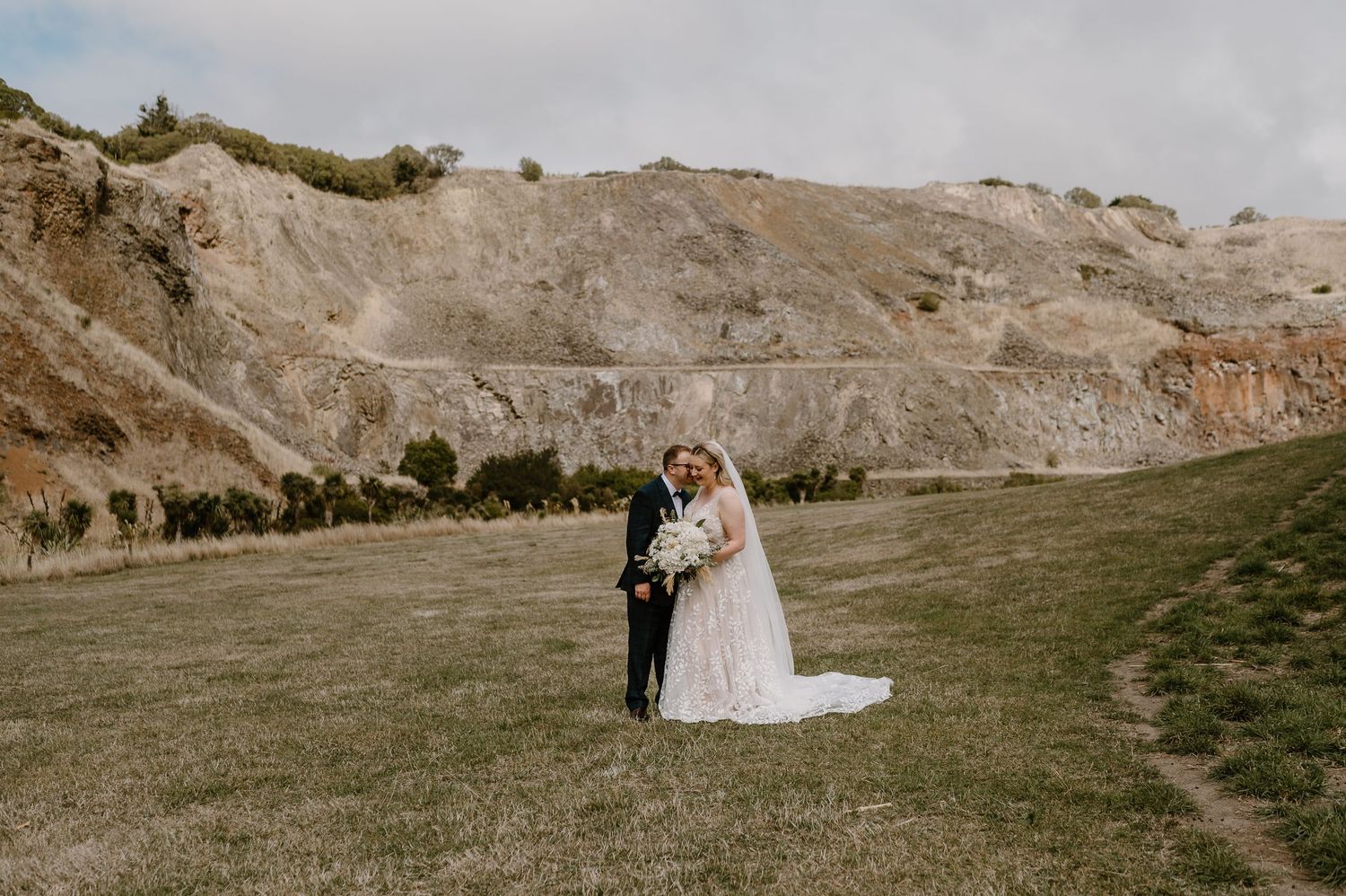 A couple shares an intimate moment during their wedding photoshoot against a scenic mountainous backdrop.