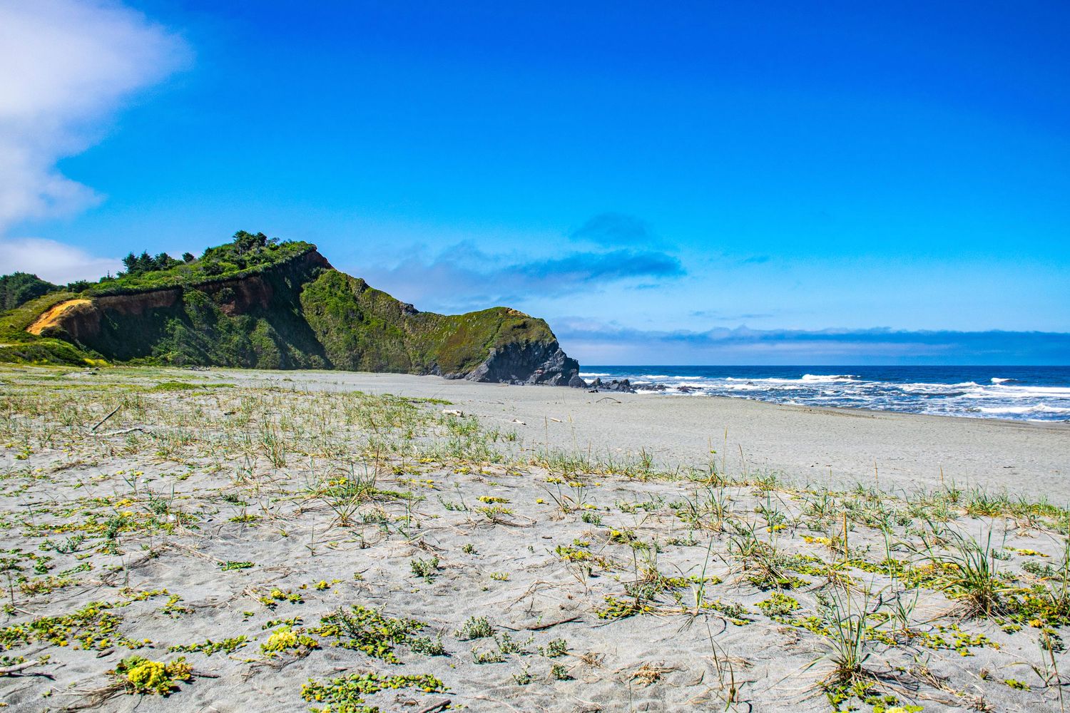 Scenic coastal beach with rocky cliffs and white sand under vibrant blue sky.