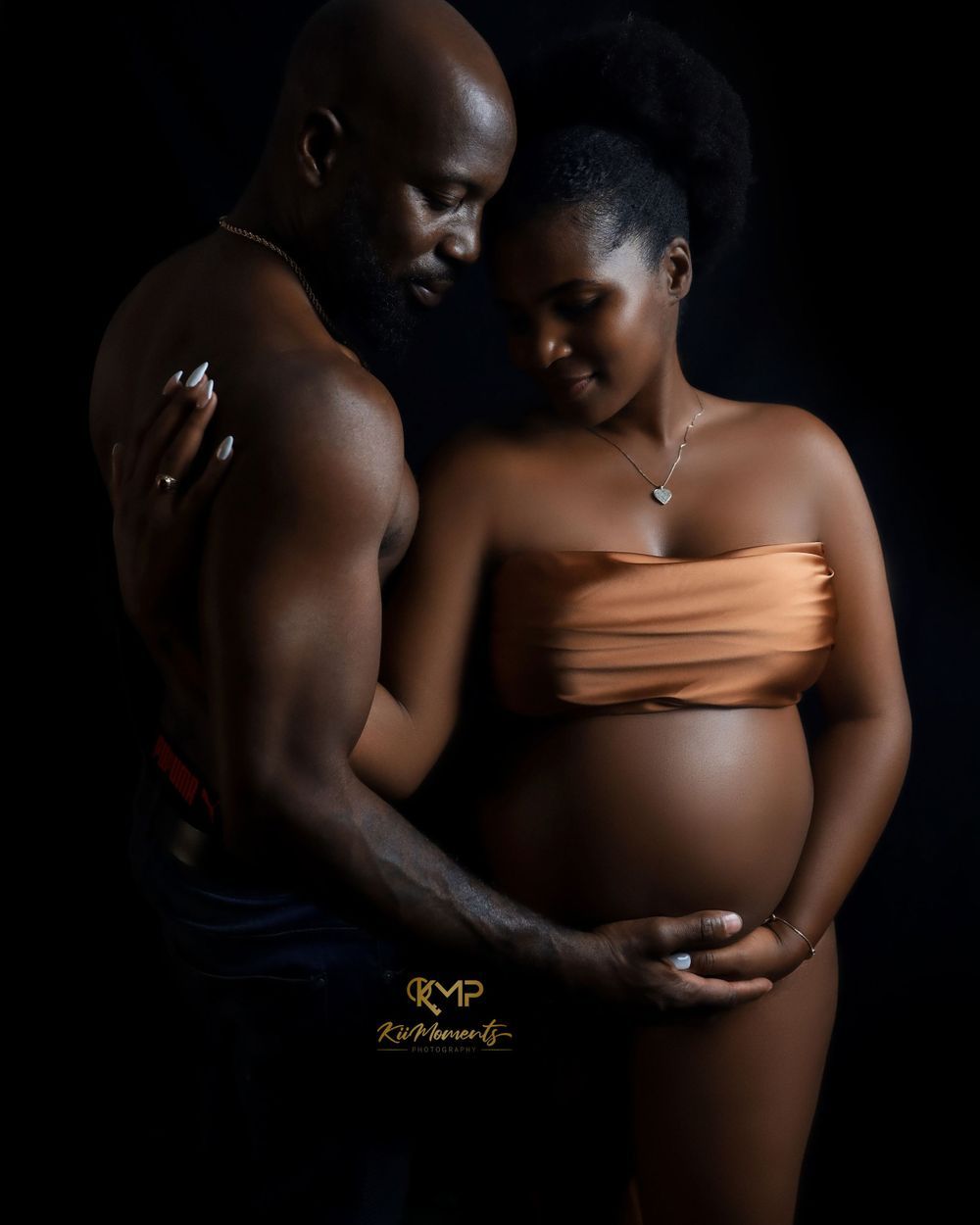 Artistic maternity photo featuring an intimate couple against dark background with woman in peach-colored top.
