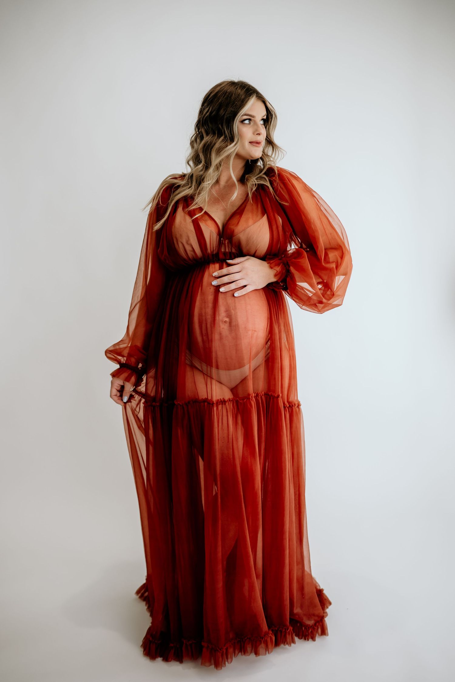 Dramatic red sheer maternity gown with billowing sleeves in studio setting.