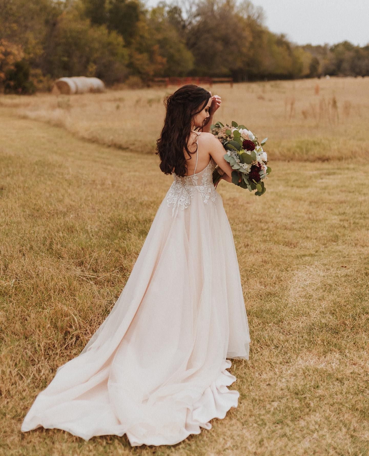 Bride in flowing white dress holds bouquet while standing in autumn field at sunset. Oklahoma Wedding Photographer