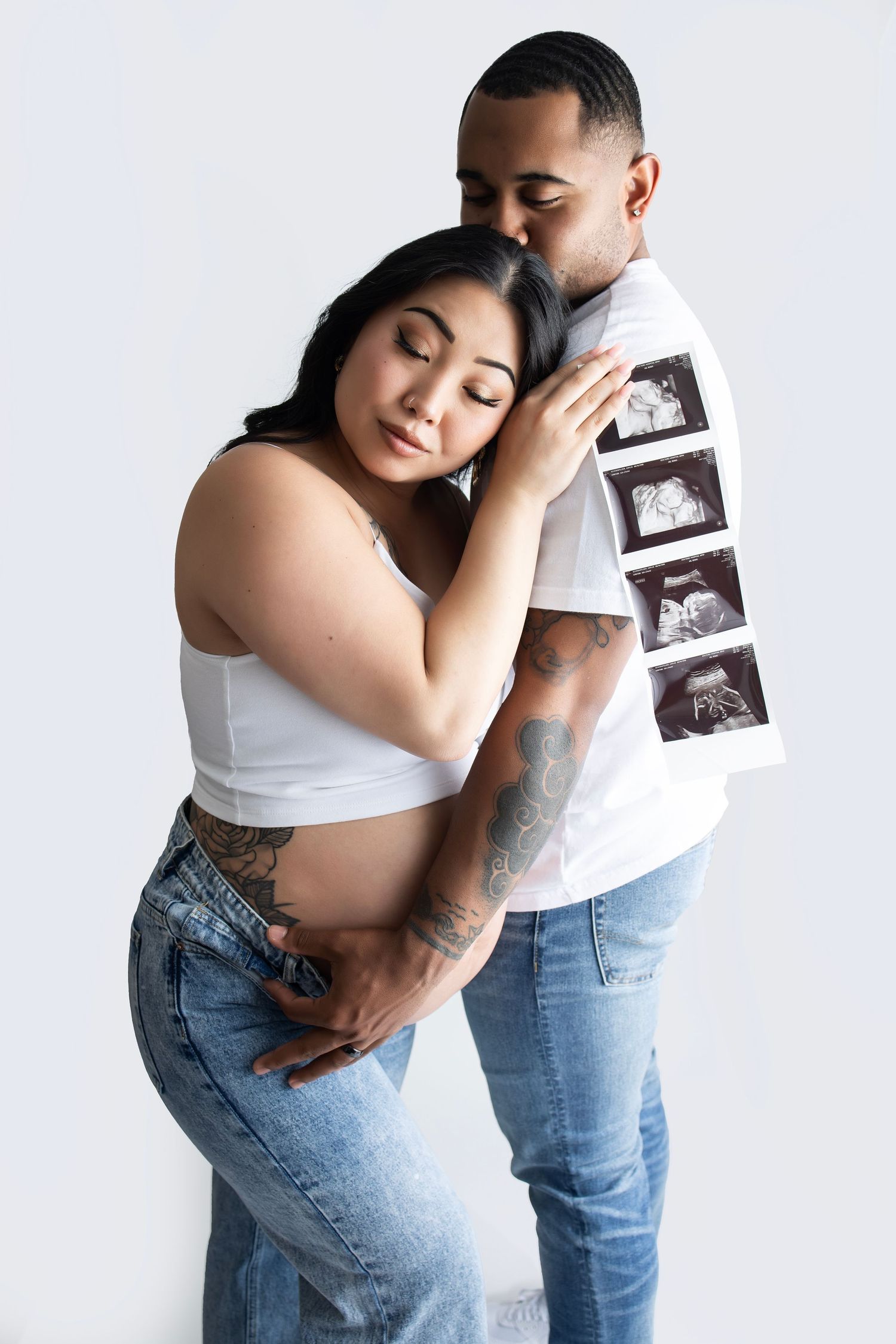 Intimate maternity portrait with ultrasound photos displayed against white background.