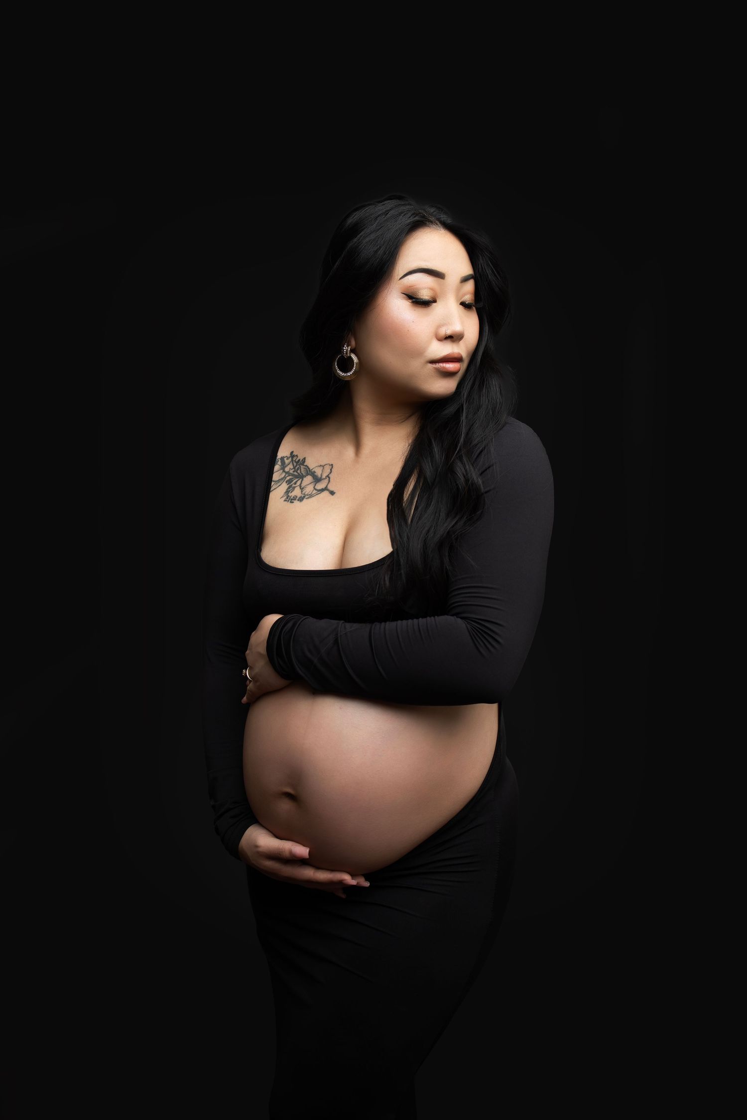 Artistic maternity portrait of woman in black dress against dark background.