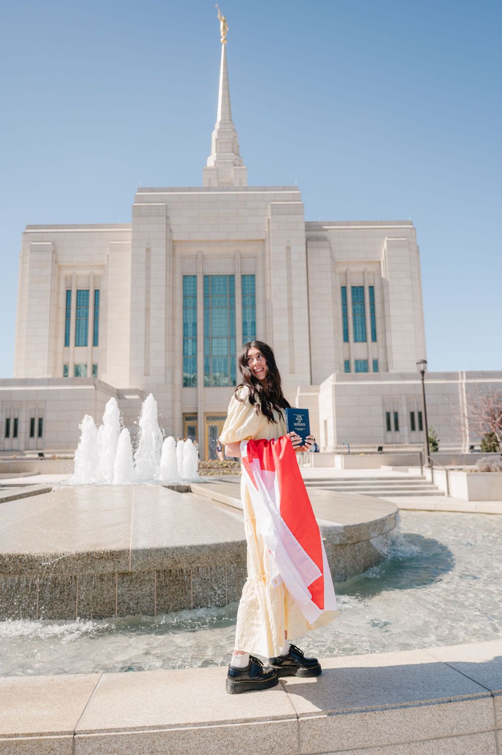 A view of a Mormon temple with its white spire and fountain in the foreground.