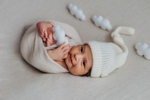 Smiling newborn in white knit hat and wrap surrounded by soft cloud decorations.
