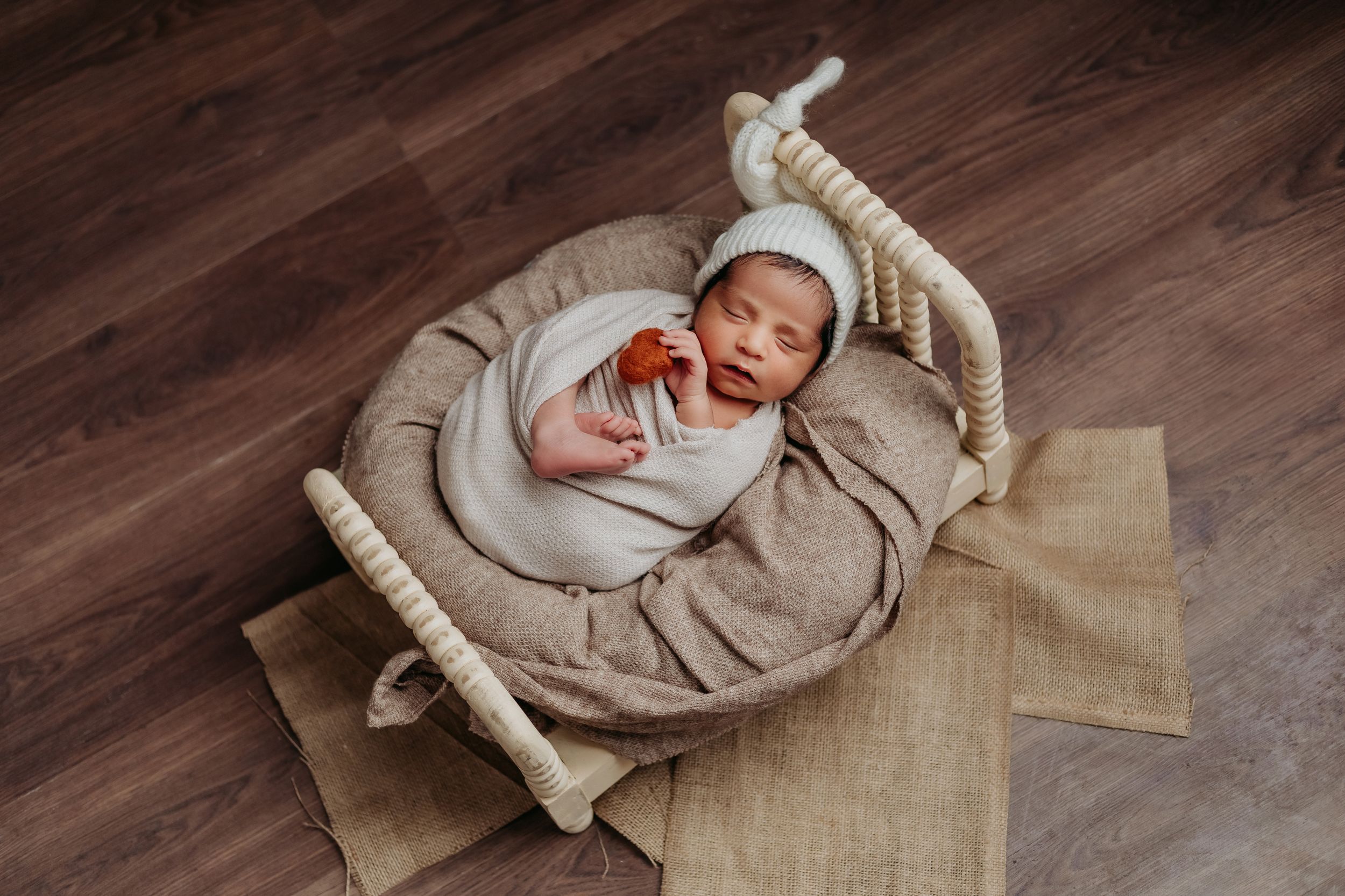 Peaceful newborn sleeping in beige wrap on rustic wooden platform with burlap accent.