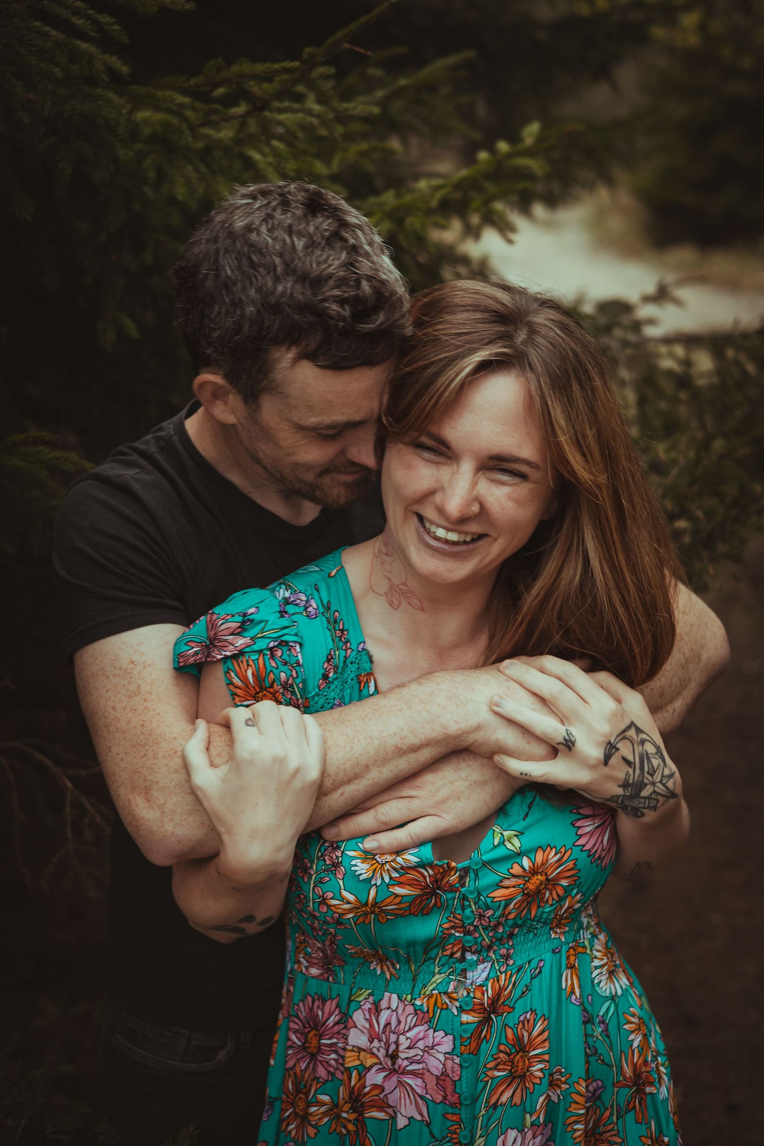 Candid engagement photos showing couple laughing and hugging in forest setting.
