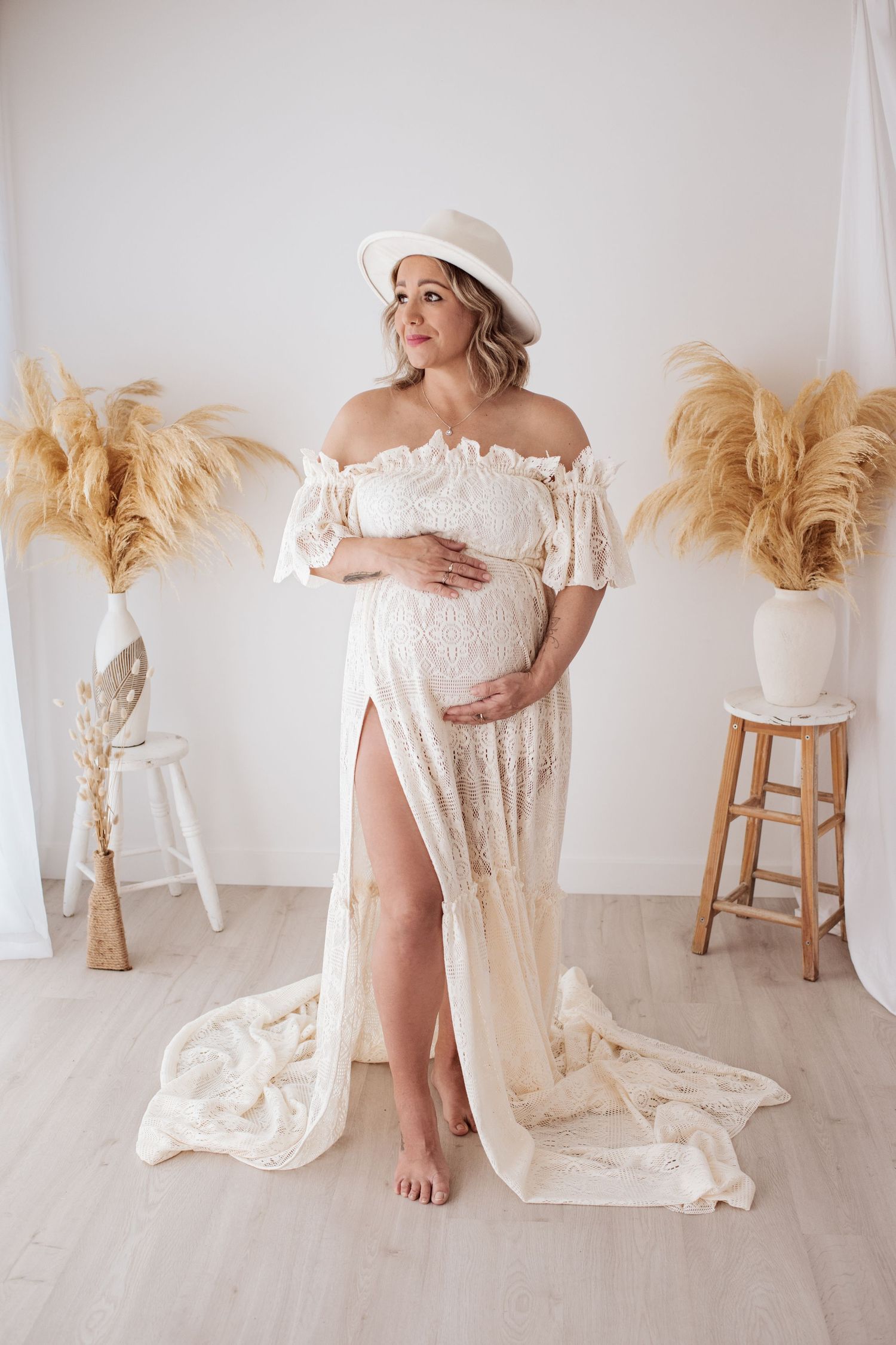 Maternity portrait in a white off-shoulder dress and sun hat with pampas grass decor.