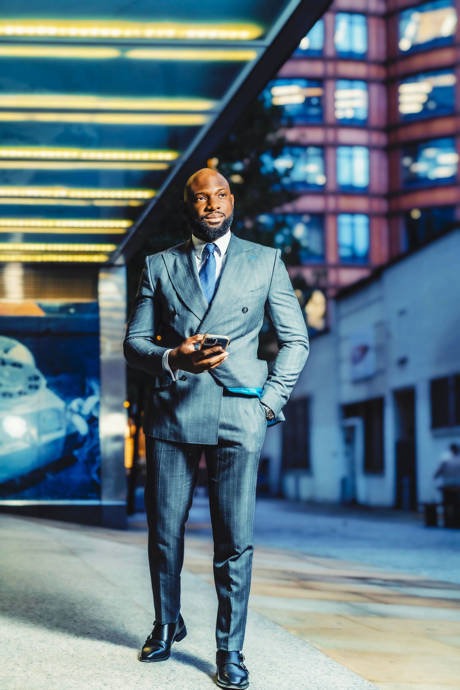 Businessman in grey suit checking phone under illuminated ceiling in urban setting.