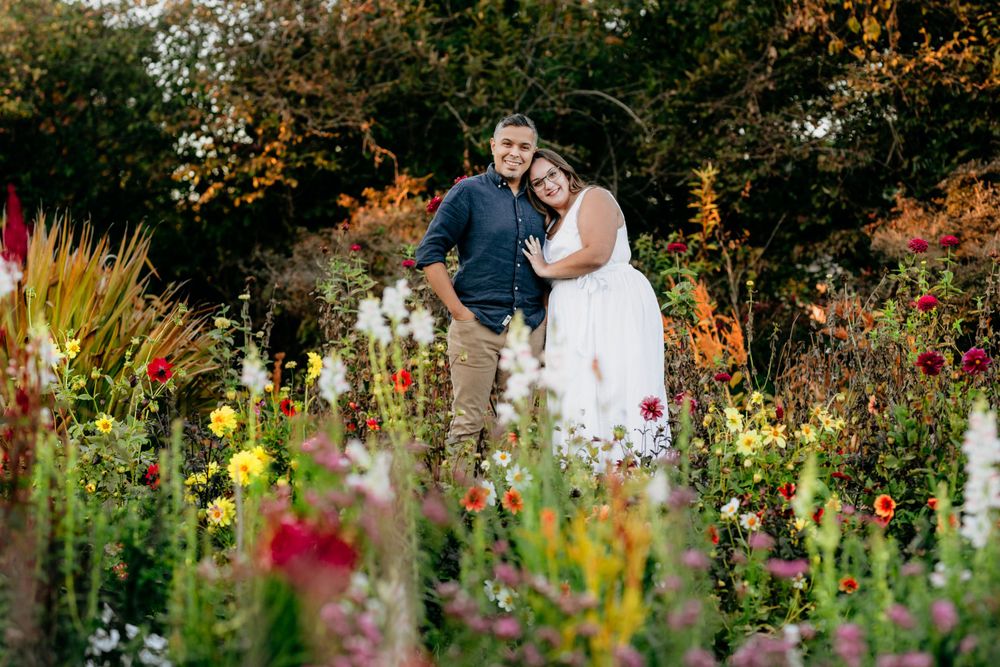 Couple poses together in a vibrant garden filled with colorful summer flowers and greenery.