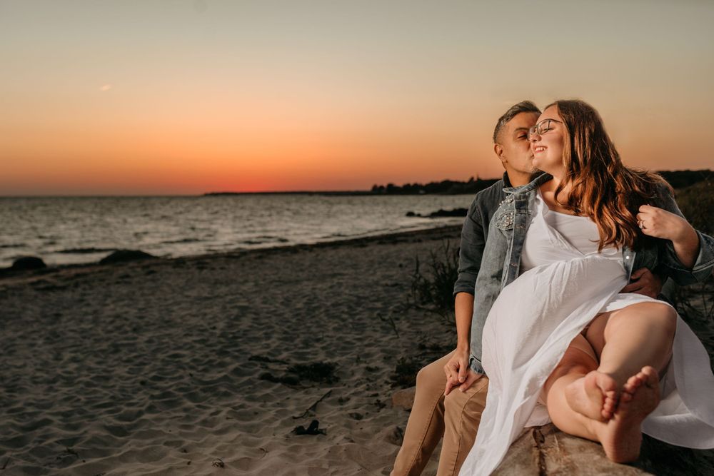 Couple shares a romantic moment on the beach at sunset with the ocean in the background.