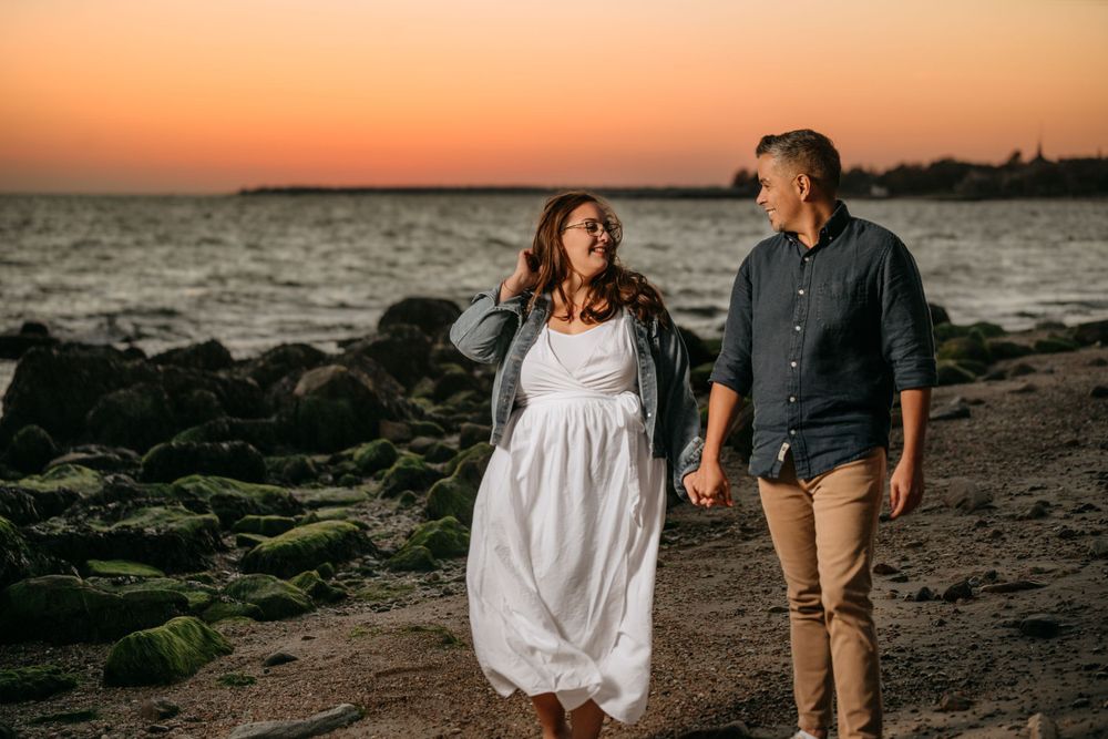 Couple strolls along rocky beach shoreline during golden hour sunset.