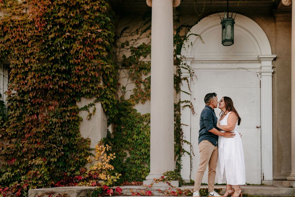 A romantic moment between a couple on an ivy-covered porch with white columns and arched doorway.
