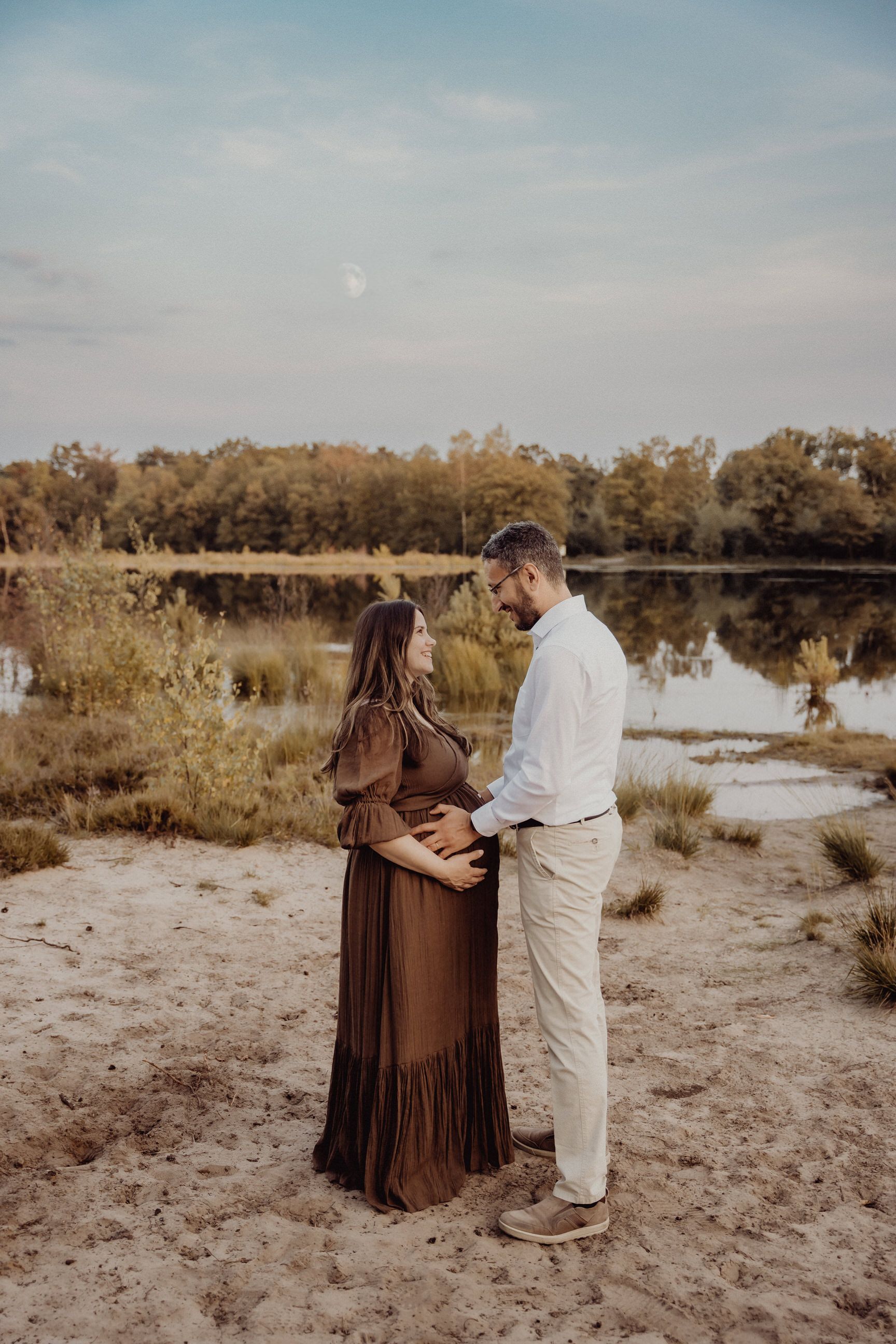 Expecting couple sharing intimate moment by lake at sunset.