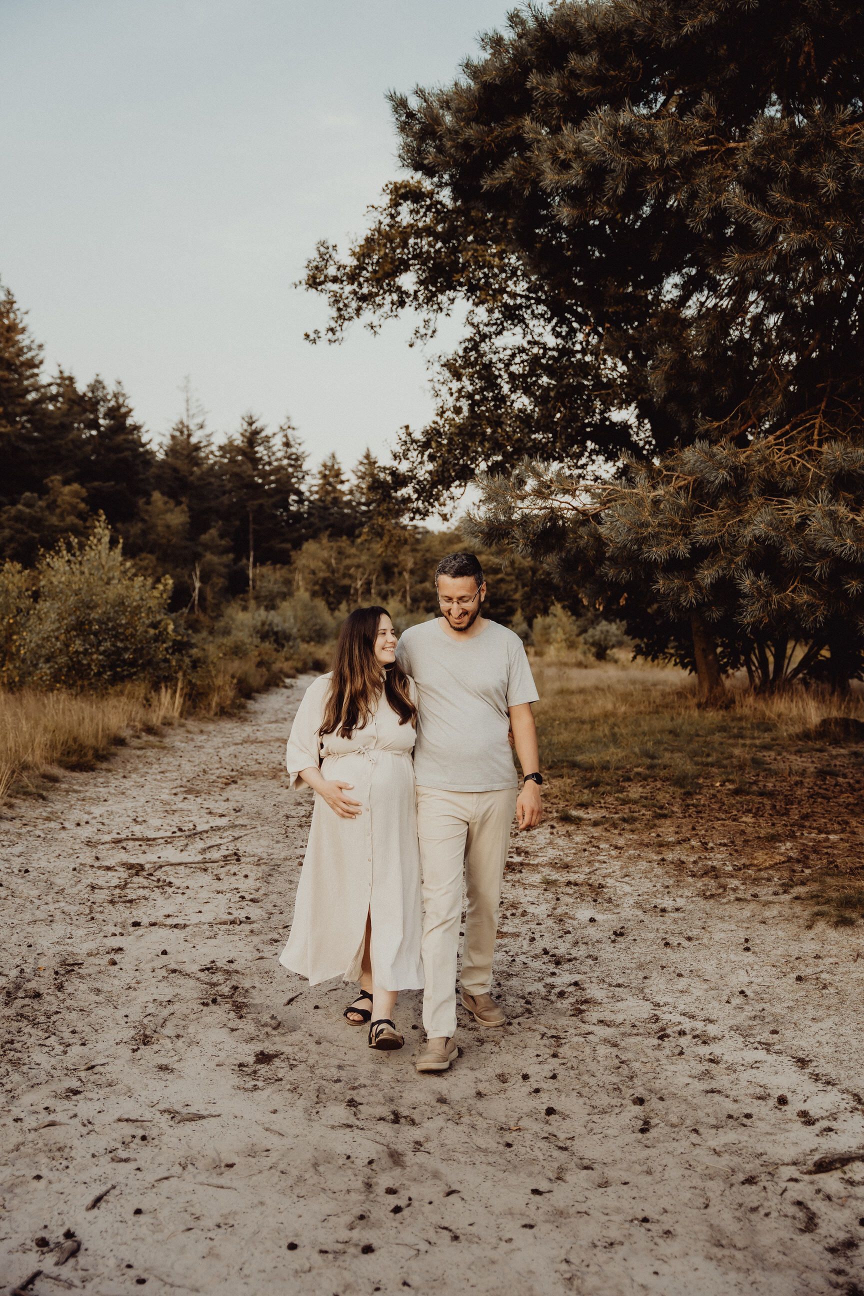 Couple walking together on sandy forest path during sunset.