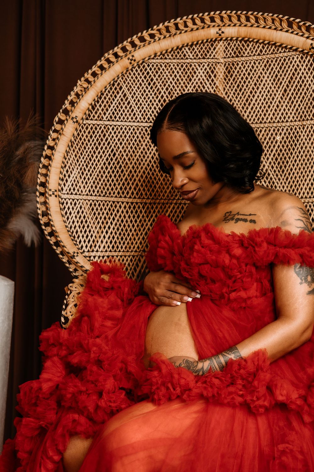 Artistic boudoir photo series featuring a red tulle dress against a dark backdrop with a wicker peacock chair.