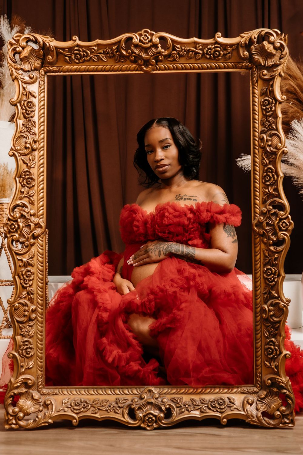 A glamorous boudoir photoshoot featuring a red tulle gown and ornate gold baroque frames against a brown backdrop.
