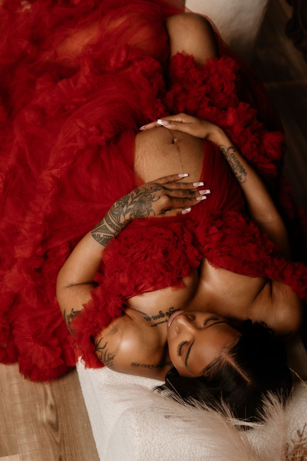 Artistic boudoir photo featuring dramatic red tulle fabric, tattoos, and elegant poses on a light wooden floor.