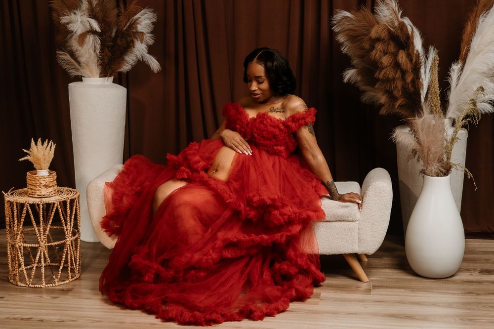 A stunning red tulle gown with ruffled layers is displayed in a romantic studio setting with white vases and decor.