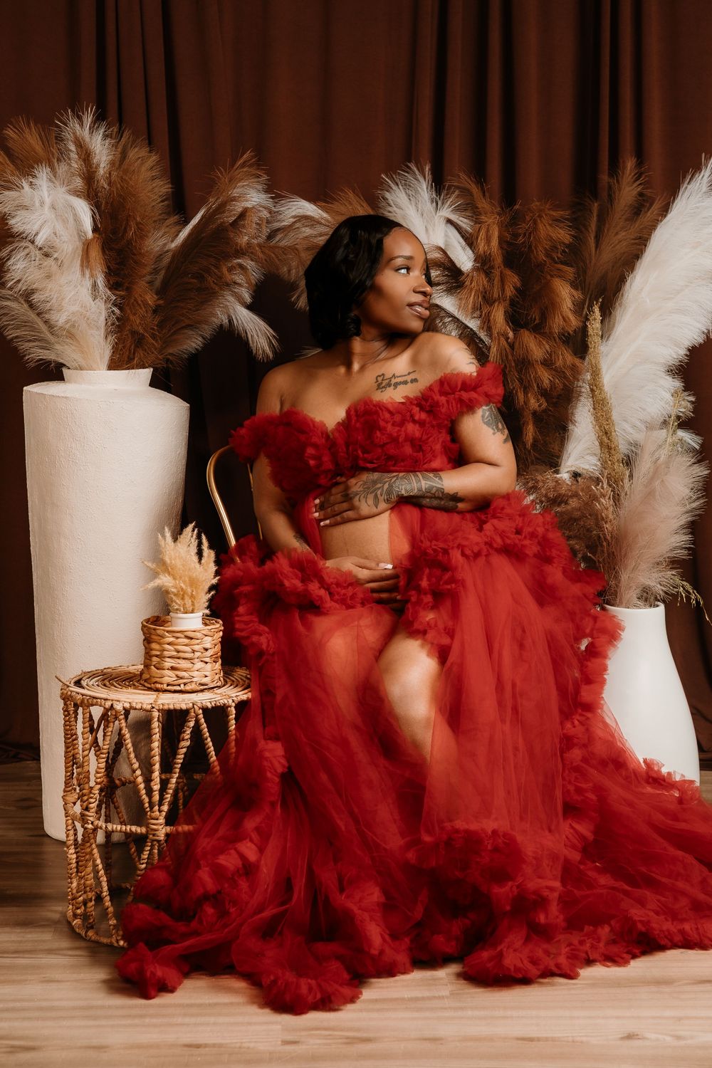 Glamorous boudoir photo featuring red tulle gown and white pampas grass decor with gold accents in warm studio lighting.