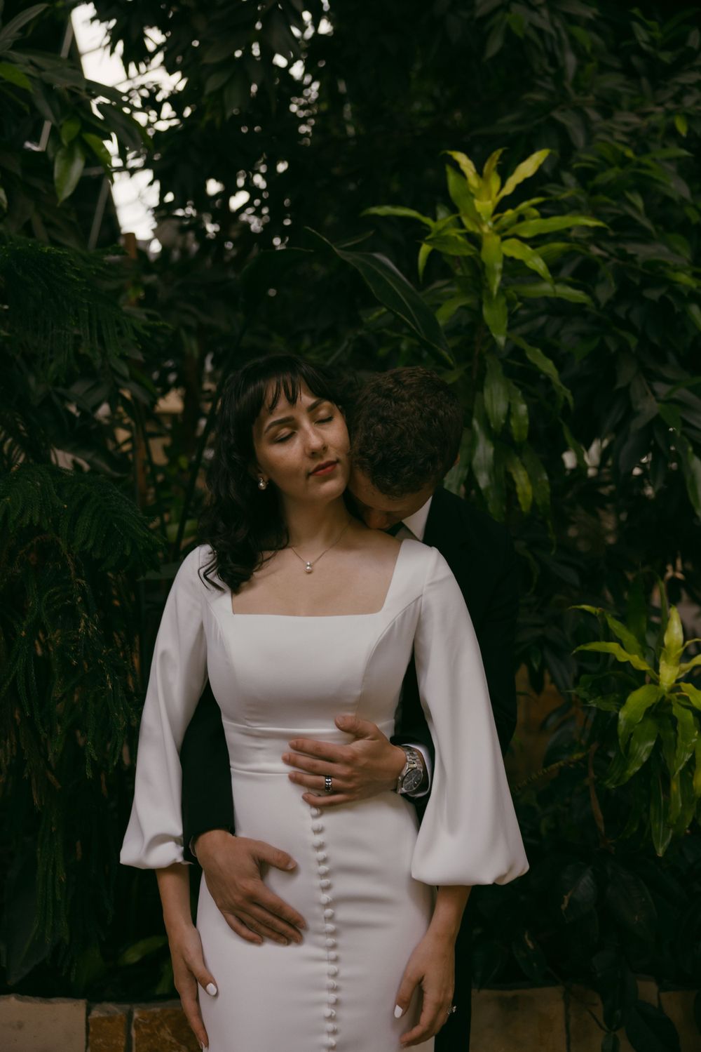Intimate couple portrait against lush foliage background.