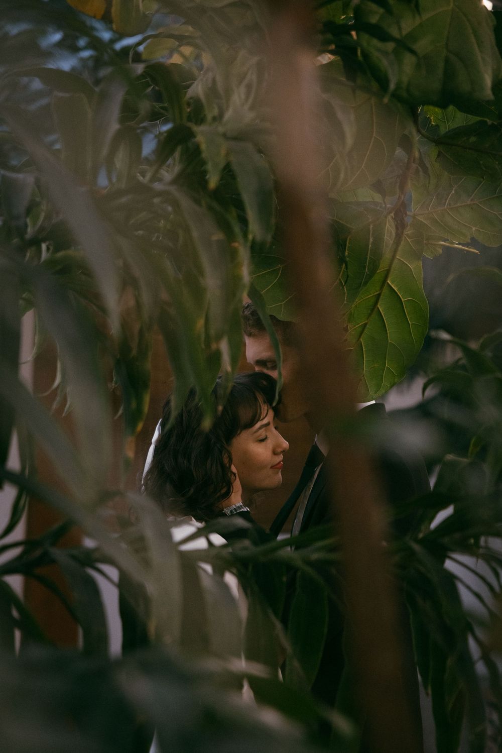 Person partially hidden behind green leaves and branches in a dreamy outdoor setting.