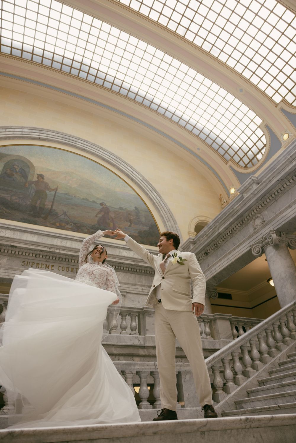 A dramatic wedding photo on marble stairs beneath a skylight and historic murals.