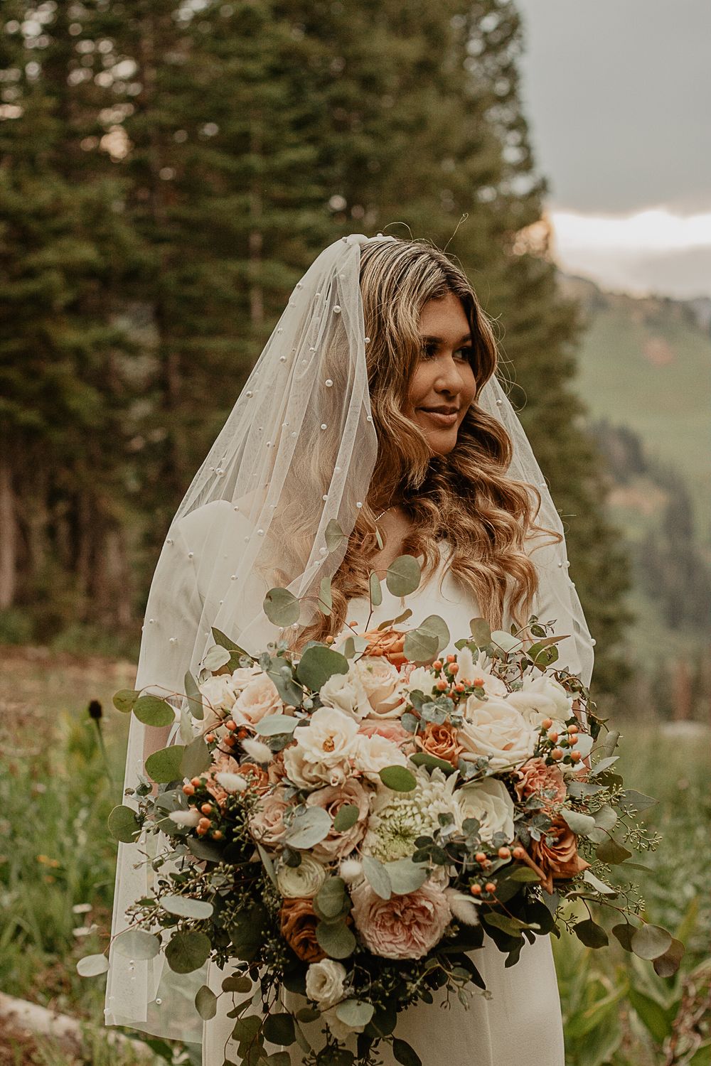 A stunning bridal portrait with a large blush and white bouquet against a mountain backdrop.