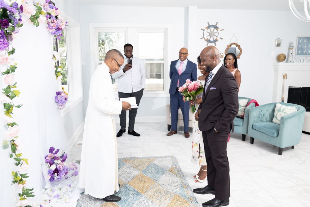 An intimate wedding ceremony taking place in a bright white room decorated with purple floral arrangements.