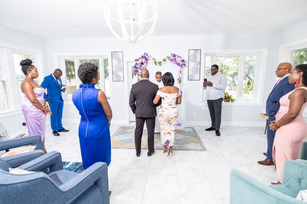 Wedding guests gathered in an elegant white room decorated with purple flowers and modern furnishings.