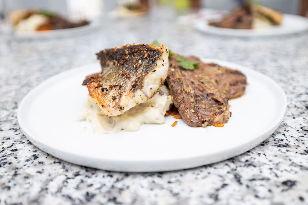 A plated gourmet meal featuring pan-seared meat and sides on a white dish atop a granite surface.